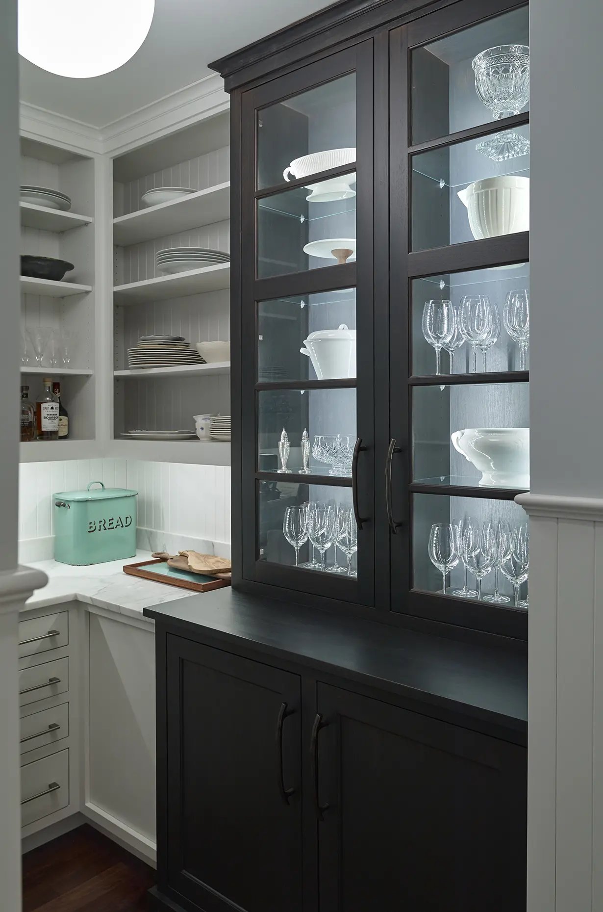 A dark hutch for storing glassware in the pantry, with white and marble accents throughout