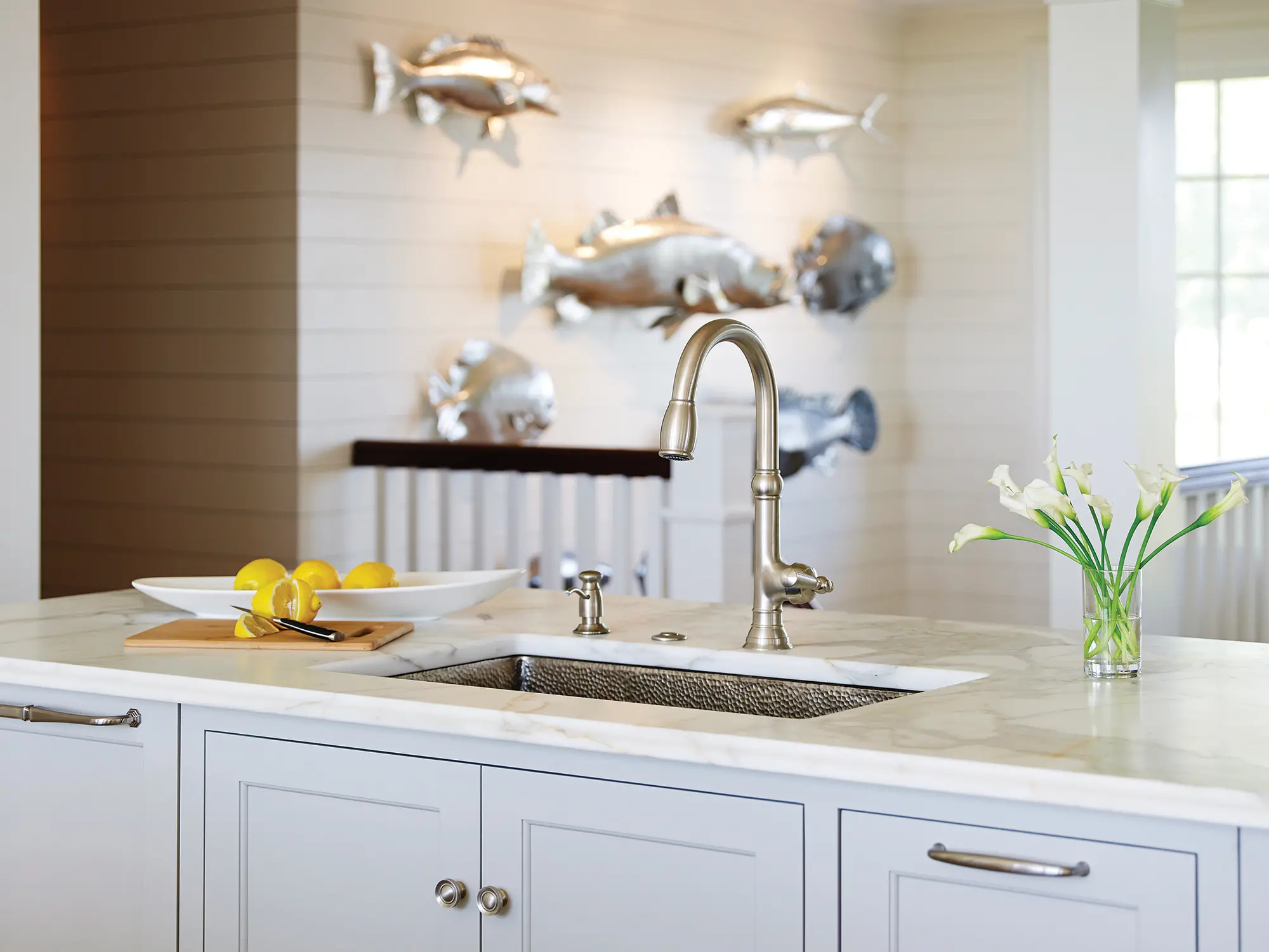 A view of the white marble countertop with hammer finished sink and steel decorative fish in the background.
