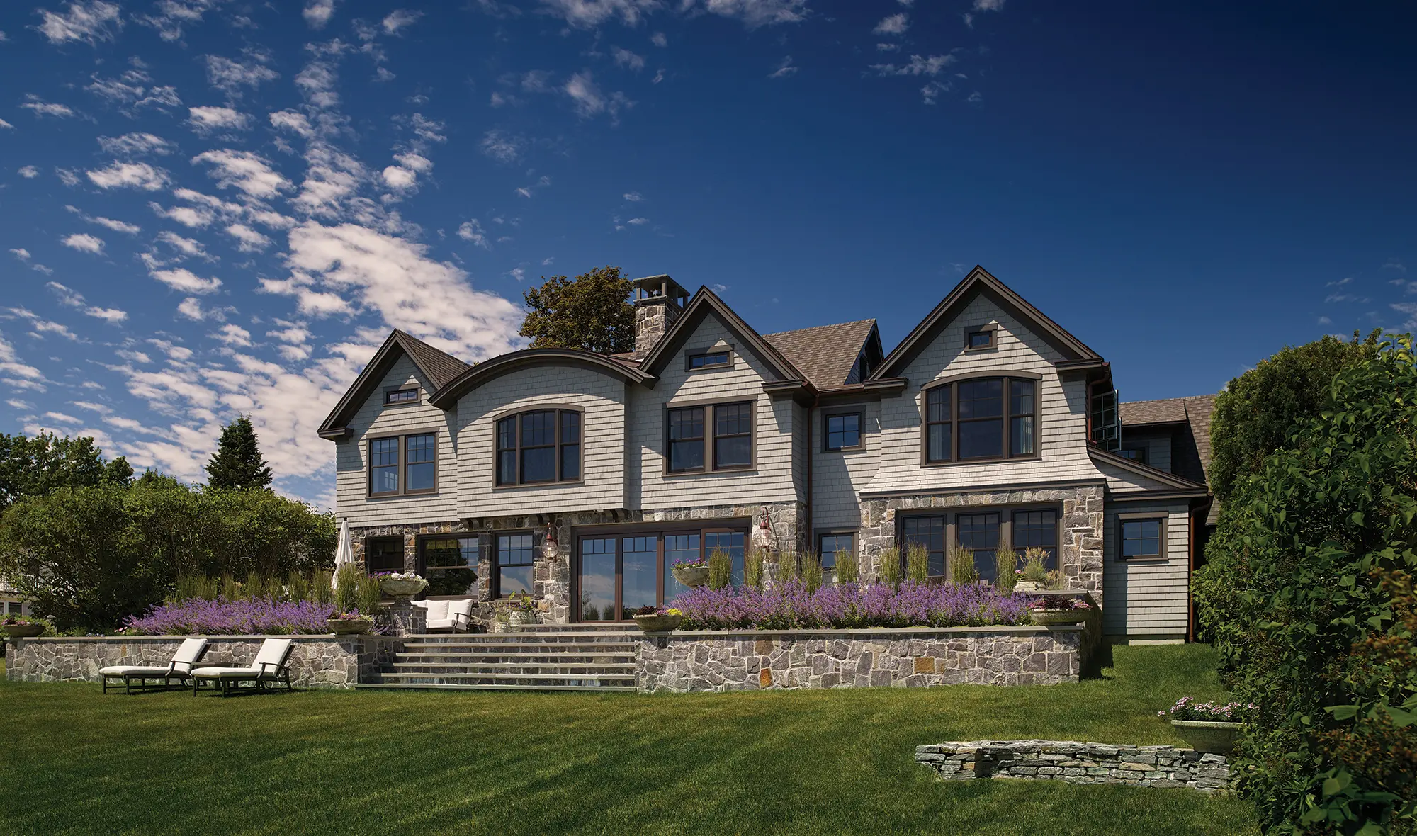 A view of the approach from the rear of the cottage with stone details, flower gardens, and a large lawn.