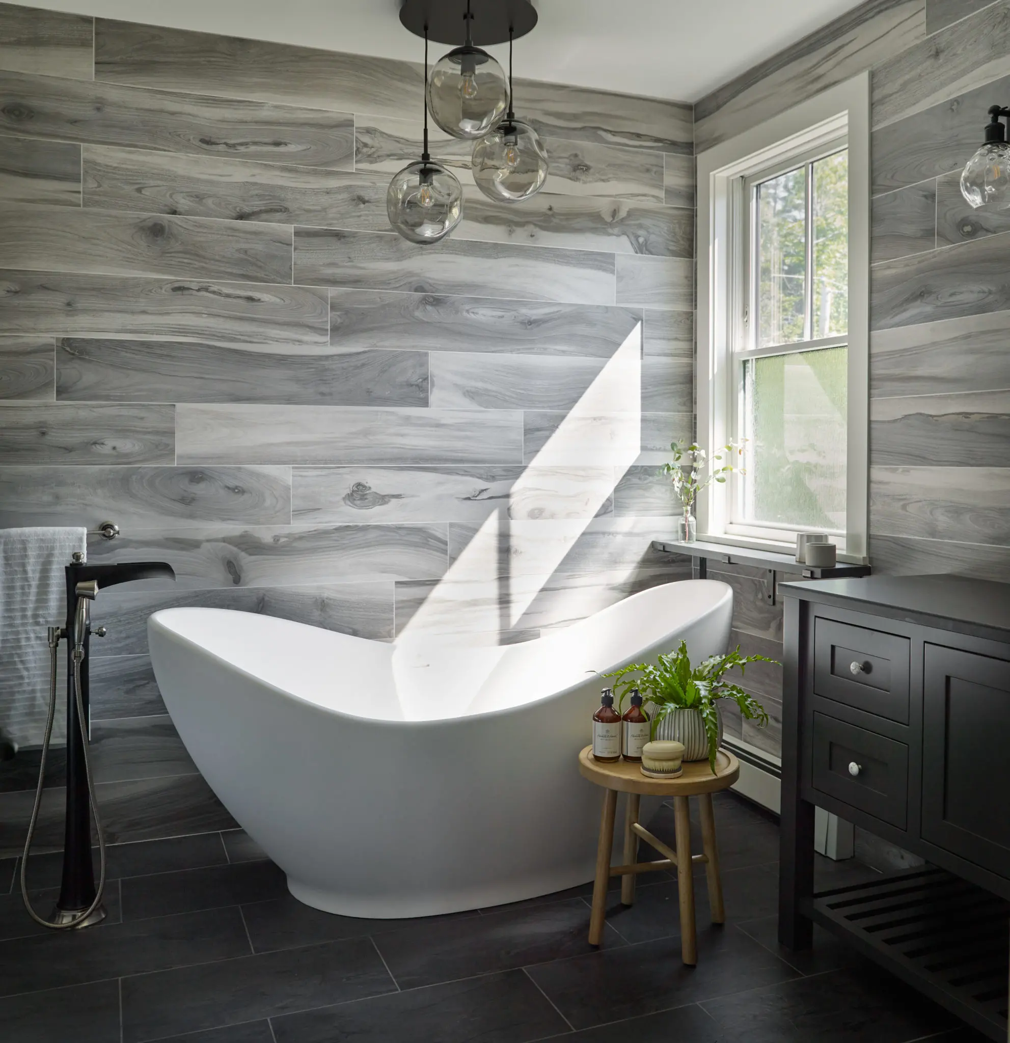 Soaking tub with freestanding faucet, modeled gray tile walls and dark gray tile floor give a spa like feel to this primary bathroom